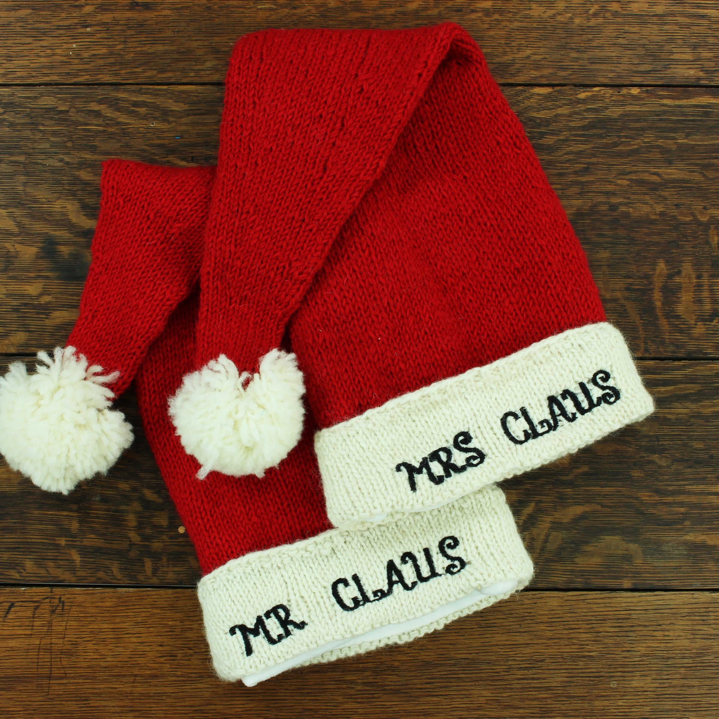 Red knitted hat with 'Mr Claus' and 'Mrs Claus' text on a wooden surface
